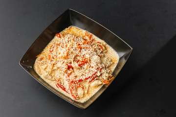  hicken with vegetables and udon noodles in a delicate creamy cheese sauce in a black bowl on a black background. Horizontal photo.
