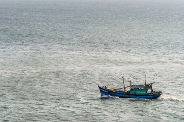 Fototapeta premium Da Nang, Vietnam - March 10, 2019: Tien Sa Port in Da Nang Bay.. Closeup of small blue and green fishing vessel returning to its harbor on gray water of bay. 