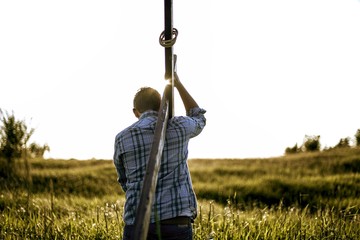 Male carrying a hand made wooden cross in a grassy field shot from behind