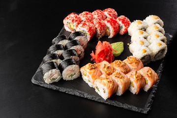 Various kinds of sushi served on black background. Sushi menu for Japanese food. Japanese sushi set. Rolls with tuna, salmon, shrimp, crab, caviar and avocado. Horizontal photo.