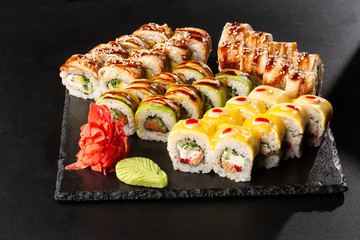 Various kinds of sushi served on black background. Sushi menu for Japanese food. Japanese sushi set. Rolls with eel, shrimp, crab, caviar, american cheese and avocado. Horizontal photo.