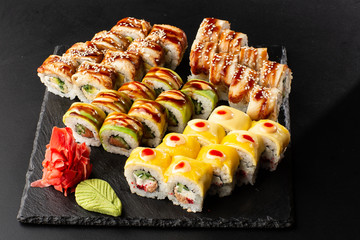 Various kinds of sushi served on black background. Sushi menu for Japanese food. Japanese sushi set. Rolls with eel, shrimp, crab, caviar, american cheese and avocado. Horizontal photo.