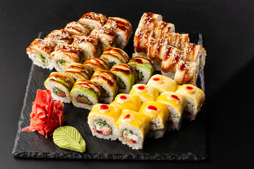 Various kinds of sushi served on black background. Sushi menu for Japanese food. Japanese sushi set. Rolls with eel, shrimp, crab, caviar, american cheese and avocado. Horizontal photo.