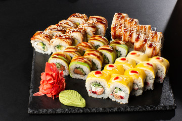 Various kinds of sushi served on black background. Sushi menu for Japanese food. Japanese sushi set. Rolls with eel, shrimp, crab, caviar, american cheese and avocado. Horizontal photo.