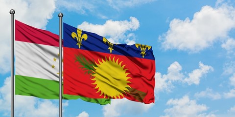 Tajikistan and Guadeloupe flag waving in the wind against white cloudy blue sky together. Diplomacy concept, international relations.