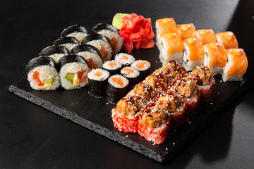 Various kinds of sushi served on black background. Sushi menu for Japanese food. Japanese sushi set. Rolls with tuna, salmon, shrimp, crab and avocado. Horizontal photo.