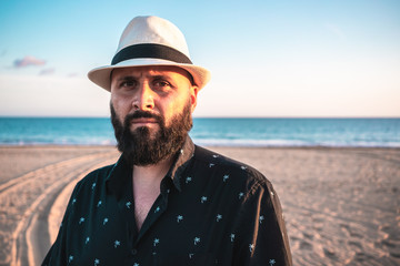 Portrait of a man with a beard and a white hat on a beach