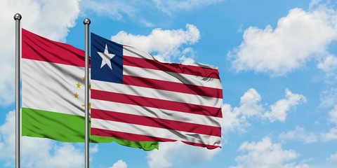 Tajikistan and Liberia flag waving in the wind against white cloudy blue sky together. Diplomacy...