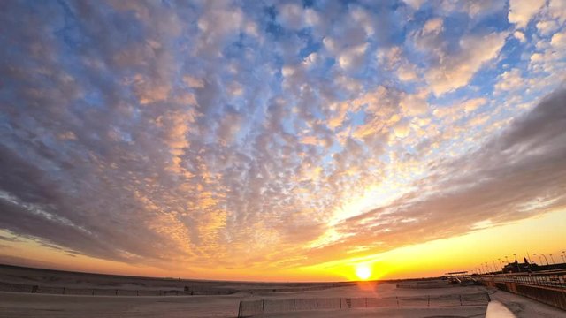 Time lapse of colorful high level clouds racing across the sky over a beach as the sun sets below the horizon. 