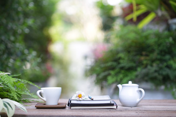 White cup and flower with white tea pot and notebooks on wooden table