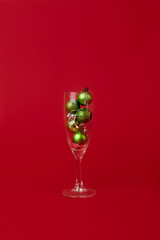 little green christmas balls lie inside a glass of champagne on a red background. Minimal style