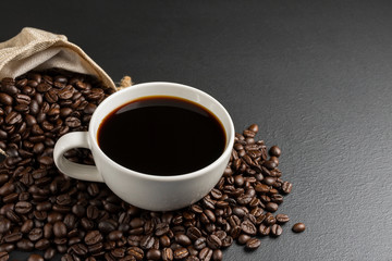 Black coffee in a white coffee cup And roasted coffee beans placed Is on the black table, the top...