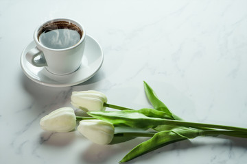 coffee background of a cup of hot black coffee with bunch of white tulip on white marble background