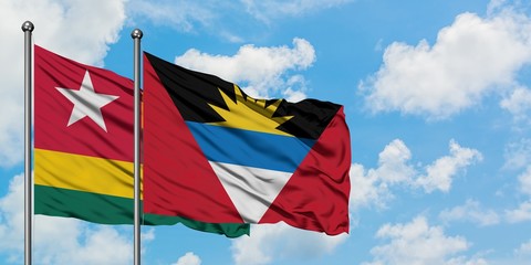 Togo and Antigua and Barbuda flag waving in the wind against white cloudy blue sky together....