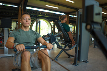 Fototapeta na wymiar young athletic and attractive man training body building doing rowing exercise in row machine pulling hard with determination and energy at gym club