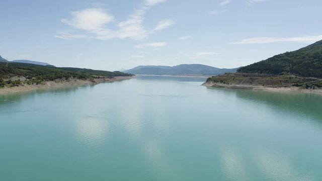Aerial Drone shot of beautiful blue turquoise Lake Yesa with water reflections near spanish mountains in Spain, blue sky, clouds and trees landscape, valley, volcanic, green nature, 4K. Tracking in.
