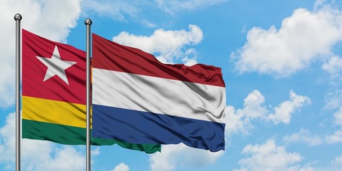 Togo and Netherlands flag waving in the wind against white cloudy blue sky together. Diplomacy...
