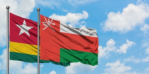 Togo and Oman flag waving in the wind against white cloudy blue sky together. Diplomacy concept, international relations.