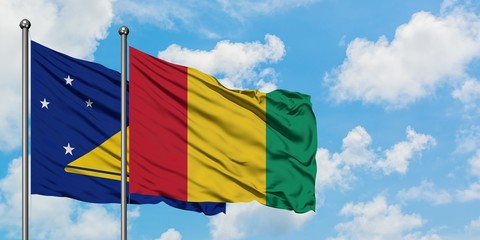 Tokelau and Guinea flag waving in the wind against white cloudy blue sky together. Diplomacy concept, international relations.