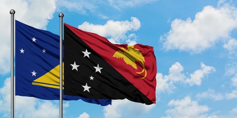 Tokelau and Papua New Guinea flag waving in the wind against white cloudy blue sky together. Diplomacy concept, international relations.