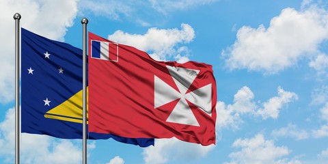 Tokelau and Wallis And Futuna flag waving in the wind against white cloudy blue sky together....