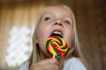 Funny child with candy lollipop, lifestyle photo of happy blonde little girl eating colorful sugar...