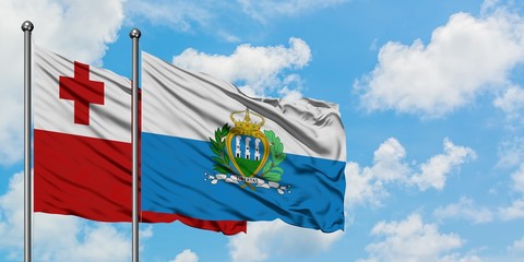 Tonga and San Marino flag waving in the wind against white cloudy blue sky together. Diplomacy concept, international relations.