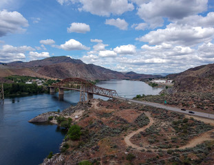 Great Aerial Photography of Beebe Bridge with a painfully blue sky and bright cumulus clouds in a craggy mountain setting with the Columbia River outside Chelan Washington