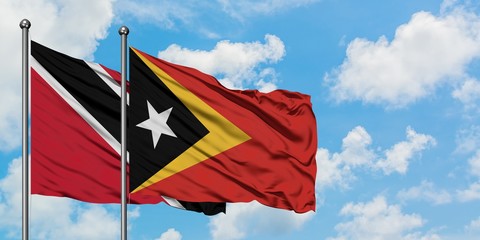 Trinidad And Tobago and East Timor flag waving in the wind against white cloudy blue sky together. Diplomacy concept, international relations.