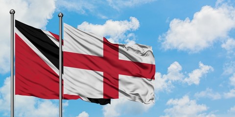 Trinidad And Tobago and England flag waving in the wind against white cloudy blue sky together....