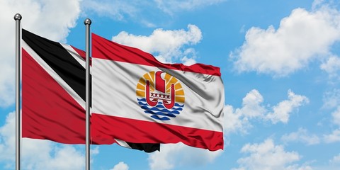 Trinidad And Tobago and French Polynesia flag waving in the wind against white cloudy blue sky together. Diplomacy concept, international relations.