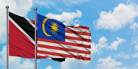 Trinidad And Tobago and Malaysia flag waving in the wind against white cloudy blue sky together. Diplomacy concept, international relations.