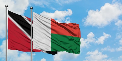 Trinidad And Tobago and Madagascar flag waving in the wind against white cloudy blue sky together. Diplomacy concept, international relations.