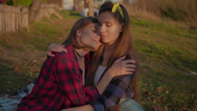 Affectionate pretty women hugging each other enjoying sensitive idyllic moments of love sitting on the grass in beautiful nature. Romantic happy female couple.