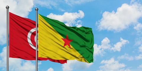 Tunisia and French Guiana flag waving in the wind against white cloudy blue sky together. Diplomacy concept, international relations.