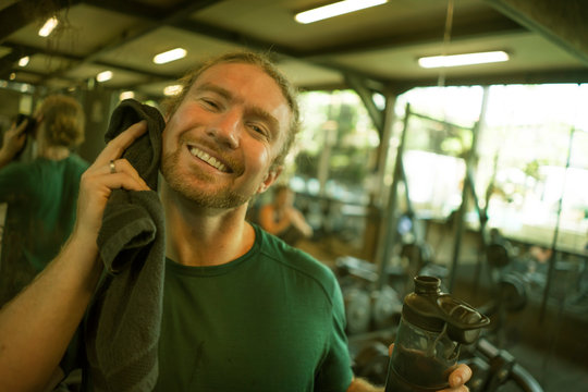 natural fitness lifestyle portrait of young happy and attractive man training wiping the sweat with towel at gym smiling cheerful  after hard bodybuilding workout