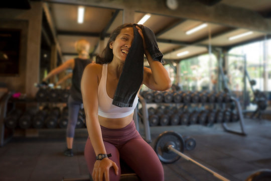 natural fitness club lifestyle portrait of young happy and attractive Asian woman training at gym bench wiping the sweat with towel smiling cheerful and positive