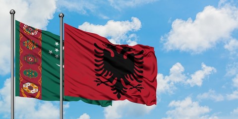 Turkmenistan and Albania flag waving in the wind against white cloudy blue sky together. Diplomacy...