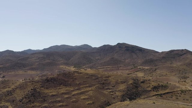 Aerial Drone shot of dry empty spanish desert with vegetation and mountains in Andalusia, Tabernas desert afternoon. Blue sky, Almeria, spain, western, far west, Sierra Nevada. Slow tracking in. 4K.