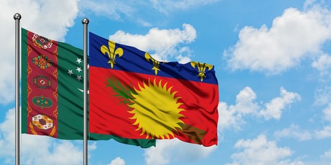 Turkmenistan and Guadeloupe flag waving in the wind against white cloudy blue sky together....