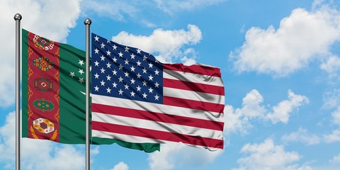 Turkmenistan and United States flag waving in the wind against white cloudy blue sky together. Diplomacy concept, international relations.