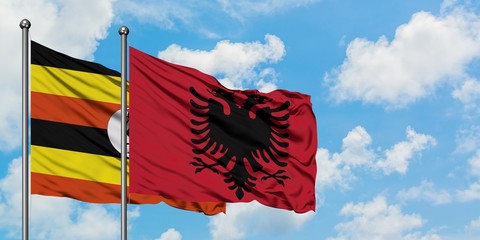 Uganda and Albania flag waving in the wind against white cloudy blue sky together. Diplomacy...