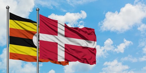 Uganda and Denmark flag waving in the wind against white cloudy blue sky together. Diplomacy...