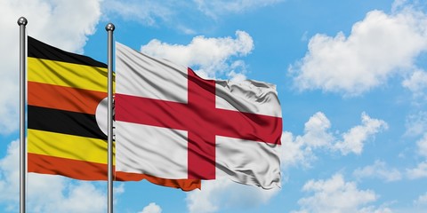Uganda and England flag waving in the wind against white cloudy blue sky together. Diplomacy...