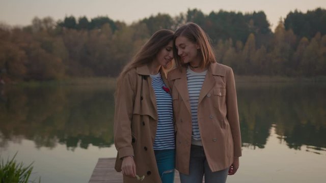 Couple of appealing lovable girlfriends hugging walking together on bridge at spring lake. Adorable positive lesbian women spending time outdoor at river bank.