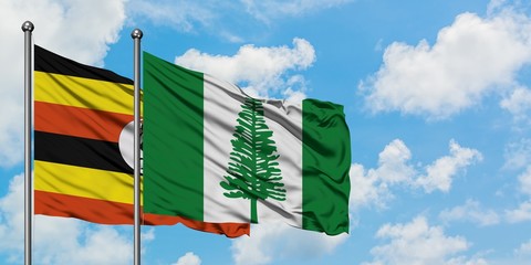 Uganda and Norfolk Island flag waving in the wind against white cloudy blue sky together. Diplomacy...