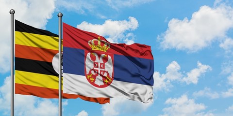 Uganda and Serbia flag waving in the wind against white cloudy blue sky together. Diplomacy concept, international relations.
