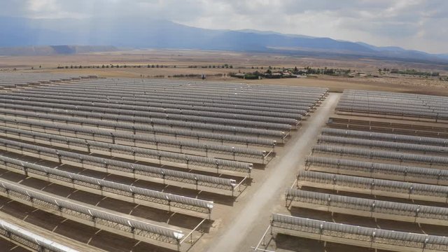 Aerial drone footage of thousands solar energy modules or panels farm, at the dry Sierra Nevada Desert, Spain. Big Photovoltaic PV Plant 4K UHD. Tracking in wide view. Side tracking. Wind turbines.