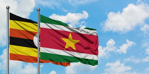 Uganda and Suriname flag waving in the wind against white cloudy blue sky together. Diplomacy...