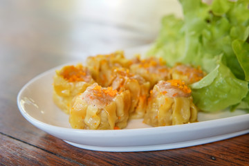 Selective focus of Chinese Steamed Dumpling topped with Flying fish roe on white dish served with lettuce leaves.